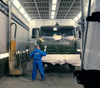 Paint booth for heavy vehicles with worker in blue suit performing painting work. Visible truck during painting process.